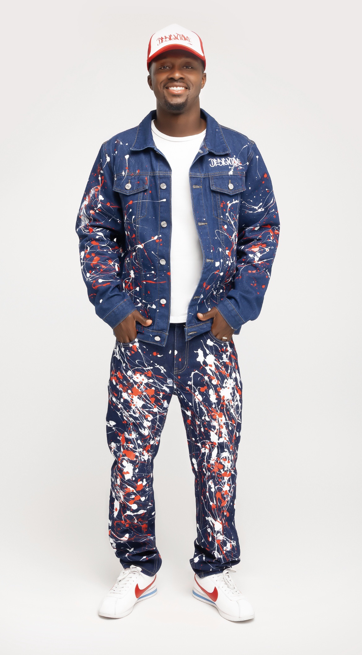 Anthony Jones in a hand paint-splattered denim jacket and jeans set with a red trucker hat
